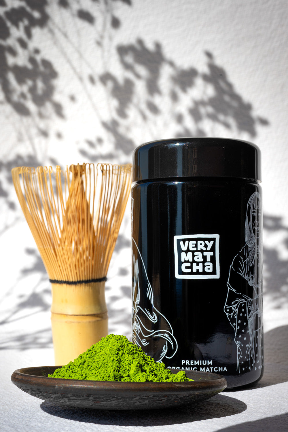 Bio Ceremonial Grade Matcha von VERY MATCHA im schwarzen Violettglas, daneben Bambusbesen (Chasen) und leuchtend grünes Matcha-Pulver – traditionell aus Tencha, 28 Tage beschattet und in Granitmühlen gemahlen.