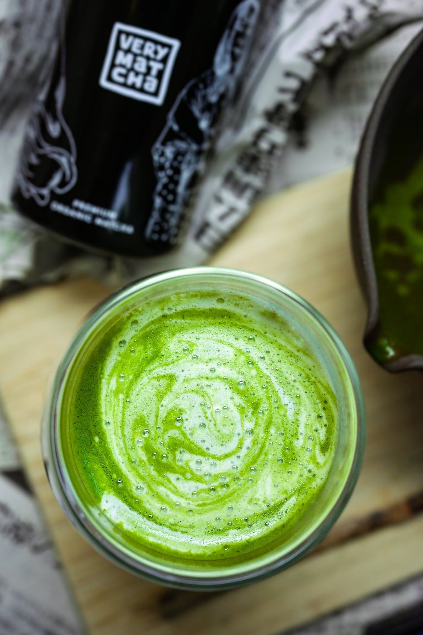Leuchtend grüner Matcha Latte mit cremiger Schaumstruktur, serviert in einem Glas, daneben die Verpackung von Very Matcha Premium Bio Matcha.