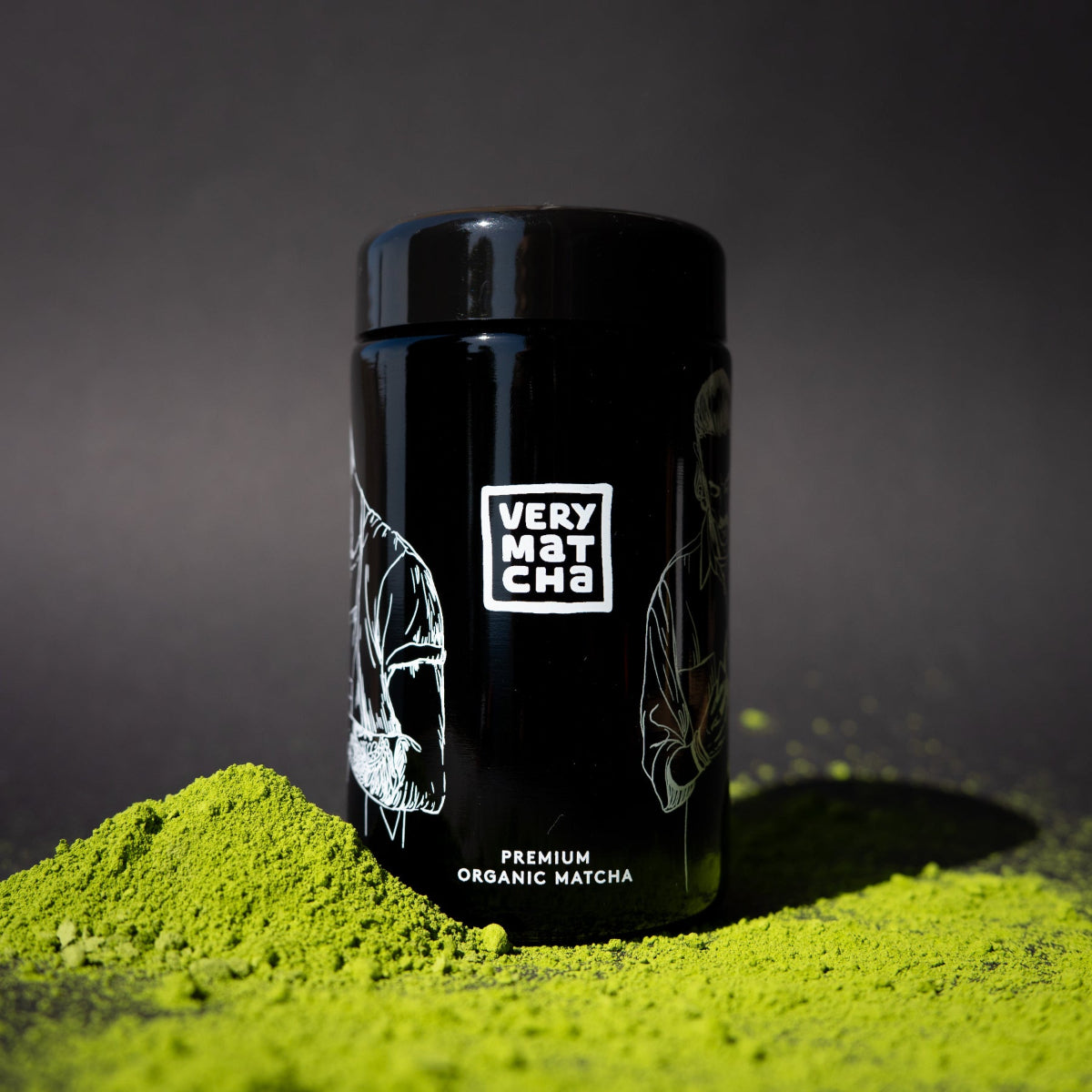 Bio Matcha Pulver mit schwarzem Very Matcha Glas im Vordergrund auf dunklem Hintergrund.