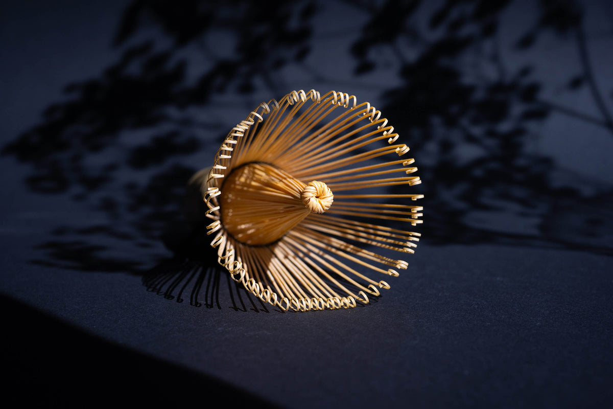 Traditioneller japanischer Matcha-Besen (Chasen) aus Bambus, von oben fotografiert mit Schattenwurf auf dunklem Hintergrund