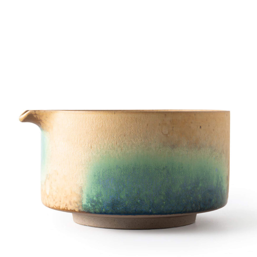 Matcha Schale AURORA mit Ausgießer in seitlicher Perspektive, verlaufende Glasur von warmem Beige zu tiefem Grünblau.